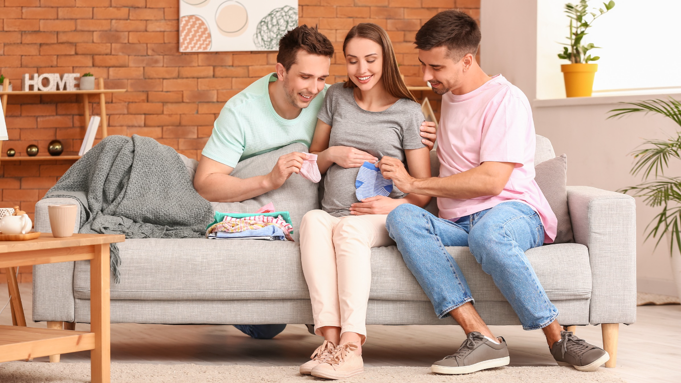 Two LGBTQ men and their gestational carrier sitting on a gray couch